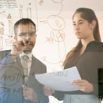 content-african-american-manager-writing-chart-glass-board-professional-young-pretty-female-colleague-holding-document-looking-graph-conference-room-teamwork-marketing-concept